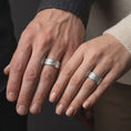 Load image into Gallery viewer, The polished silver flower wedding band is worn on a finger, showing the repeating floral details, smooth edges, and refined unisex spinner ring design in a premium lifestyle photograph.