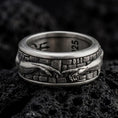 Load image into Gallery viewer, An oxidized sterling silver Creation of Adam spinner ring rests on dark volcanic rock, showing sculpted reaching hands, textured wall details, and a wide symbolic band in a macro studio close-up.