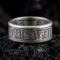 Load image into Gallery viewer, An oxidized sterling silver Aztec spinner ring rests on dark volcanic rock, showing engraved geometric panels, dark recessed details, and a wide symbolic band in a macro studio close-up.