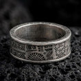Load image into Gallery viewer, An oxidized sterling silver Aztec spinner ring rests on dark volcanic rock, showing geometric panels, stepped motifs, tribal-inspired symbols, and dark recessed engravings in a macro studio close-up.