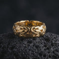 Load image into Gallery viewer, A gold plated Byzantine chain band ring rests on rugged volcanic rock, featuring interwoven chain-inspired links, strong sculptural depth, and a substantial unisex ring profile in a luxury macro studio close-up.