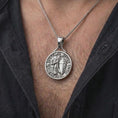 Load image into Gallery viewer, The polished silver crusader necklace is worn naturally on the neck, showing the armored knight, sword, detailed shield, castle backdrop, and substantial sterling silver pendant design in a premium lifestyle photograph.