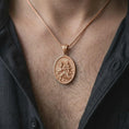 Load image into Gallery viewer, The rose gold plated St. Christopher pendant is worn on the chest, showcasing the sculpted religious figures, oval medal shape, flowing water details, and timeless Christian travel protection jewelry design.