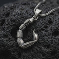 Load image into Gallery viewer, An oxidized sterling silver scorpion tail pendant rests on dark volcanic rock, showing articulated segmented sections, textured edges, a curved stinger, and dark recessed details in a dramatic macro studio close-up.