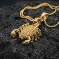 Load image into Gallery viewer, A gold plated scorpion necklace rests on rugged volcanic rock, showcasing the realistic pincers, textured segmented body, curved tail, and bold Scorpio zodiac symbolism in a luxury macro studio close-up.