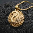 Load image into Gallery viewer, A gold plated swan pendant rests on rugged volcanic rock, showcasing the graceful bird, layered wing feathers, flowing ornamental waves, and romantic nature-inspired jewelry design in a luxury macro photograph.