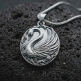 Load image into Gallery viewer, The polished sterling silver swan necklace is displayed on textured black volcanic rock, highlighting the elegant bird silhouette, sculpted feathers, curved neck, and detailed wave-inspired ornamentation.