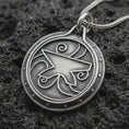 Load image into Gallery viewer, An oxidized sterling silver Zenithar-inspired amulet pendant rests on dark volcanic rock, featuring a raised geometric merchant symbol, spiral details, dotted border, and dark recessed circular background.