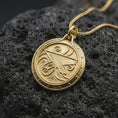 Load image into Gallery viewer, A gold plated Zenithar-inspired pendant rests on rugged volcanic rock, showcasing the bold central merchant symbol, decorative spiral elements, dotted perimeter, and fantasy artifact styling.