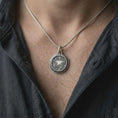 Load image into Gallery viewer, An oxidized sterling silver fantasy amulet is worn on the chest, displaying the central Zenithar-inspired symbol, dark recessed background, ornamental swirls, and substantial medallion profile.