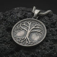 Load image into Gallery viewer, An oxidized sterling silver Tree of Life pendant rests on dark volcanic rock, featuring raised Yggdrasil branches, delicate leaves, intertwined roots, and a circular medallion with dark recessed details.