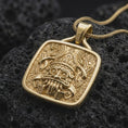 Load image into Gallery viewer, Gold plated Tlaloc pendant resting on rugged black volcanic rock, featuring the Aztec rain deity with ringed eyes, sharp fangs, and detailed Mesoamerican motifs.
