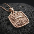 Load image into Gallery viewer, Rose gold plated Tlaloc necklace displayed on textured volcanic stone, showcasing the sculpted rain god face, detailed headdress, circular eyes, and geometric Aztec relief.