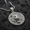 Load image into Gallery viewer, Polished sterling silver tiger head necklace displayed on dark volcanic stone, highlighting the roaring expression, sculpted stripes, fangs, and decorative medallion frame.