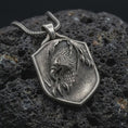 Load image into Gallery viewer, Oxidized sterling silver eagle shield pendant on black volcanic rock, featuring a detailed eagle head, layered feathers, sharp talons, and textured heraldic shield.
