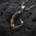 Load image into Gallery viewer, A bronze sterling silver scorpion tail pendant rests on dark volcanic rock, showing articulated segmented sections, textured edges, a curved stinger, and dark recessed details in a dramatic macro studio close-up.