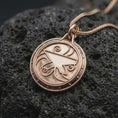 Load image into Gallery viewer, The rose gold plated fantasy amulet is arranged on black volcanic rock, emphasizing the raised geometric emblem, flowing spiral accents, circular medallion shape, and detailed RPG-inspired design.