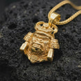 Load image into Gallery viewer, A gold plated King Gorilla Samurai necklace rests on rugged black volcanic rock, showcasing the sculpted gorilla head, curved samurai helmet horns, decorative crown, and detailed warrior armor.