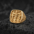 Load image into Gallery viewer, Gold plated Crucifixion ring resting on black volcanic rock, featuring Jesus Christ at Calvary between the two thieves, INRI inscription, three crosses, and detailed religious scenery.