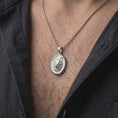 Load image into Gallery viewer, Polished silver wolf head pendant worn on the chest, featuring a realistic wolf portrait, sculpted fur details, and bold wildlife-inspired oval necklace design.