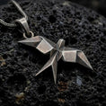 Load image into Gallery viewer, Oxidized sterling silver origami swallow pendant on black volcanic rock, featuring sharp geometric folds, pointed wings, and a faceted flying bird silhouette.