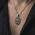 Load image into Gallery viewer, Oxidized sterling silver dragon shield necklace worn on the chest, showing the coiled winged dragon, textured shield background, and bold medieval fantasy pendant profile.