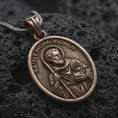 Load image into Gallery viewer, Bronze sterling silver Saint Homobonus medal necklace on black volcanic rock, featuring the haloed Catholic saint holding a staff with SAINT HOMOBONUS lettering.