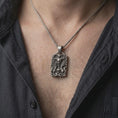 Load image into Gallery viewer, Oxidized sterling silver horned skull necklace worn on the chest, displaying the large curled horns, screaming skull, skeletal hands, and gothic flame details.