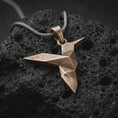 Load image into Gallery viewer, Bronze origami hummingbird pendant on black volcanic rock, featuring a geometric folded bird design with a long pointed beak and angular wings.