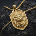 Load image into Gallery viewer, Gold plated roaring lion pendant resting on black volcanic rock, featuring an aggressive lion portrait, sharp canine teeth, flowing mane, and bold medieval-inspired shield design.