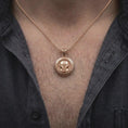 Load image into Gallery viewer, Rose gold plated Mandalorian helmet pendant worn on the chest, showcasing the raised bounty hunter helmet, engraved lettering, symbolic insignia bail, and bold space fantasy necklace aesthetic.