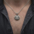 Load image into Gallery viewer, Oxidized sterling silver Mandalorian helmet necklace worn on the chest, showing the detailed bounty hunter mask, circular Star Wars medallion, and bold sci-fi inspired pendant design.