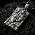 Load image into Gallery viewer, Oxidized sterling silver Gemini twins pendant on black volcanic rock, featuring two sculpted faces resting together, detailed facial expressions, and an intricate geometric rectangular frame.