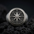 Load image into Gallery viewer, Oxidized sterling silver compass rose signet ring on black volcanic rock, featuring a raised eight-point compass star, engraved directional markings, and a detailed circular navigation dial.
