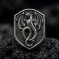 Load image into Gallery viewer, Oxidized sterling silver dragon shield signet ring on black volcanic rock, featuring a raised winged dragon with curved horns, detailed scales, spread wings, and a long coiled tail.