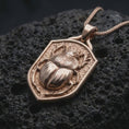 Load image into Gallery viewer, Rose gold plated beetle shield necklace displayed on textured volcanic stone, showcasing the dimensional stag beetle sculpture, intricate body textures, branching mandibles, and raised shield border.
