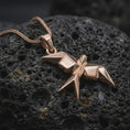 Load image into Gallery viewer, Rose gold plated geometric swallow necklace displayed on textured volcanic stone, showcasing the folded-paper inspired form, angular wings, and minimalist sculptural design.