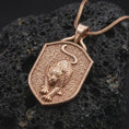 Load image into Gallery viewer, Rose gold plated leopard pendant displayed on dark textured stone, showcasing the raised big cat sculpture, detailed facial features, spotted body, extended paws, and distinctive shield-shaped animal jewelry centerpiece.