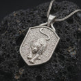 Load image into Gallery viewer, Polished sterling silver leopard pendant displayed on dark volcanic rock, highlighting the three-dimensional wild cat sculpture, detailed spotted coat, muscular shoulders, focused eyes, and raised shield-shaped silver frame.