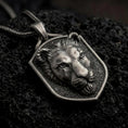 Load image into Gallery viewer, Oxidized sterling silver lioness pendant necklace on black volcanic stone, featuring a raised female lion head with detailed facial contours, textured background, shield-shaped frame, and braided silver chain.