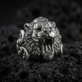 Load image into Gallery viewer, Oxidized sterling silver roaring tiger ring displayed on black volcanic stone, featuring an open mouth, sharp fangs, detailed fur texture, and bold sculptural side accents.