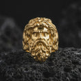 Load image into Gallery viewer, Gold plated sterling silver Poseidon ring displayed on dark volcanic rock, featuring a raised ancient Greek sea god face with an elaborate wavy beard, flowing hair, powerful facial expression, and warm gold finish.