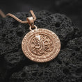 Load image into Gallery viewer, Rose gold plated Lovecraftian amulet displayed on dark volcanic stone, showcasing the raised cephalopod emblem, engraved fantasy lettering, and gothic statement pendant style.
