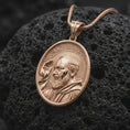 Load image into Gallery viewer, Rose gold plated Saint Pio pendant displayed on textured volcanic stone, showcasing the realistic facial relief, detailed beard, raised blessing hand, halo, and meaningful Catholic devotional jewelry design.