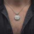 Load image into Gallery viewer, Polished silver Mandalorian pendant worn on the chest, featuring the sculpted T-visor helmet, raised lettering, and distinctive round bounty hunter necklace styling.