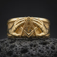 Load image into Gallery viewer, Gold plated 925 sterling silver Freemason Square and Compasses ring displayed on black volcanic rock, featuring two realistic hands surrounding the central Masonic G symbol, engraved compass arms, textured background, and warm gold plated finish.