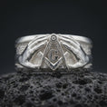 Load image into Gallery viewer, Polished 925 sterling silver Masonic ring resting on black volcanic stone, showcasing symmetrical sculpted hands surrounding a raised square and compass emblem, decorative letter G, detailed fingers, wide band, and bright polished silver finish.