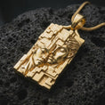 Load image into Gallery viewer, Gold plated Gemini twins pendant resting on black volcanic rock, featuring two closely positioned human faces, raised geometric patterns, and a distinctive rectangular astrology medallion.
