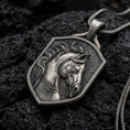 Load image into Gallery viewer, Oxidized sterling silver horse head pendant necklace resting on black volcanic stone, featuring a sculpted horse with a flowing mane, detailed leather-style bridle, expressive eyes, and a textured shield-shaped silver frame.