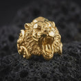 Load image into Gallery viewer, Gold plated roaring tiger ring resting on volcanic stone, highlighting the aggressive big cat face, open jaws, detailed fur strands, and bold masculine animal jewelry design.